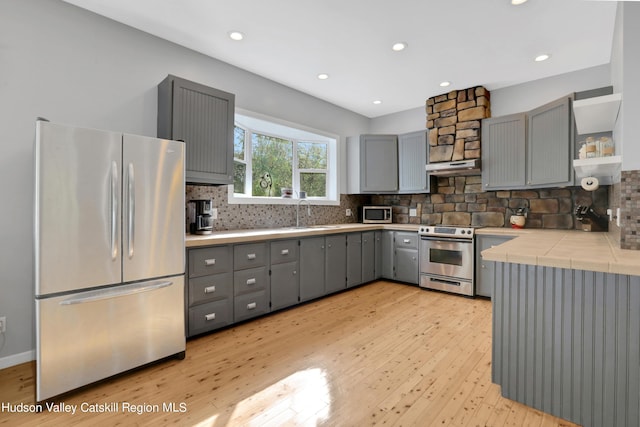 kitchen featuring gray cabinetry, backsplash, light hardwood / wood-style flooring, appliances with stainless steel finishes, and tile counters