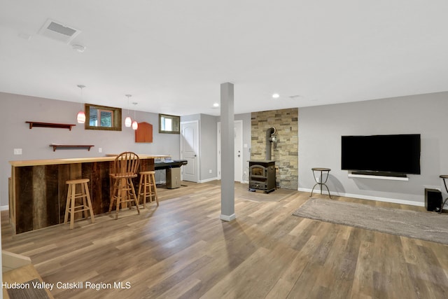 living room with indoor bar, light hardwood / wood-style flooring, and a wood stove