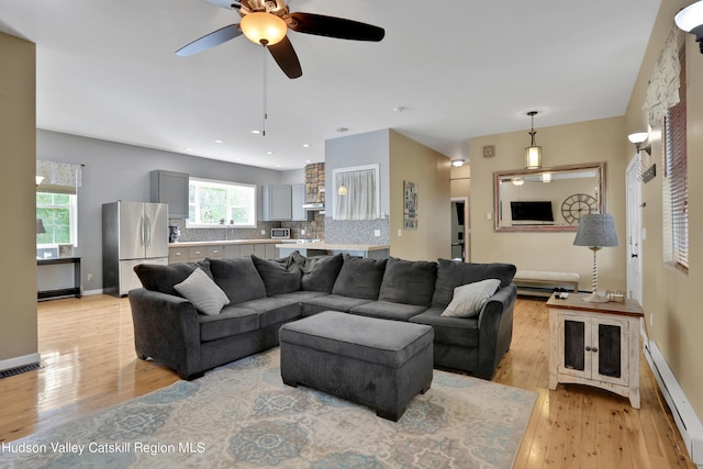 living room featuring ceiling fan, light wood-type flooring, and baseboard heating