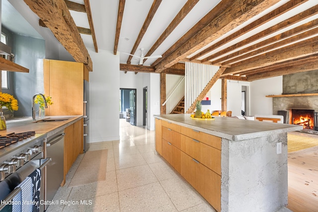 kitchen with a large fireplace, appliances with stainless steel finishes, a kitchen island, beam ceiling, and sink