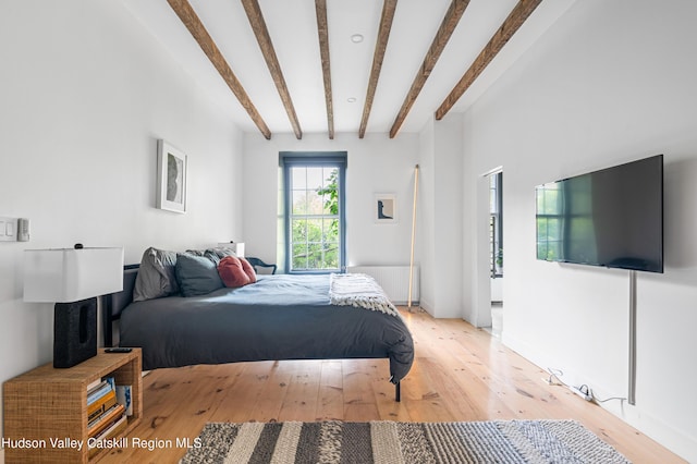 bedroom featuring beam ceiling, light hardwood / wood-style flooring, and radiator heating unit