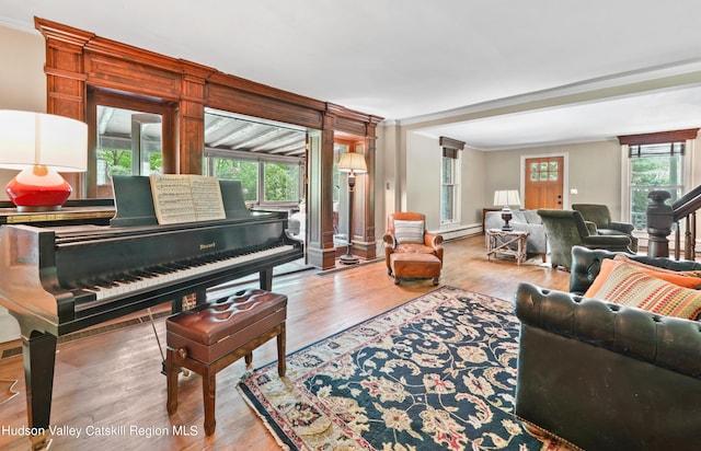 living room featuring wood-type flooring, decorative columns, baseboard heating, and crown molding