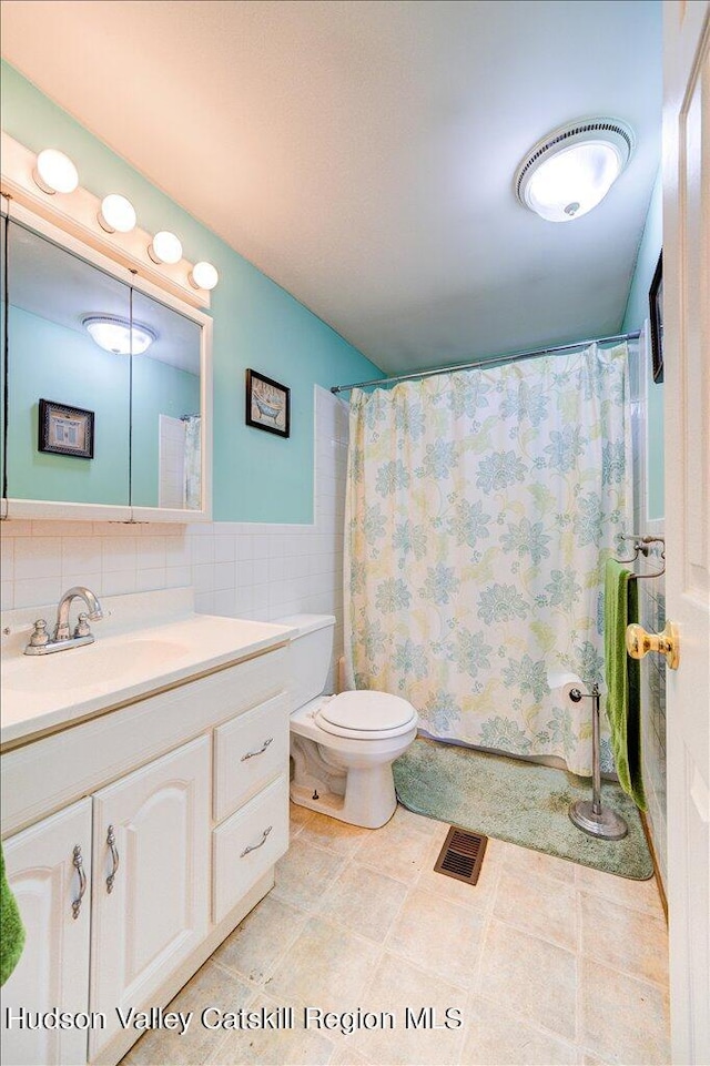 bathroom featuring curtained shower, tile patterned flooring, toilet, vanity, and tile walls