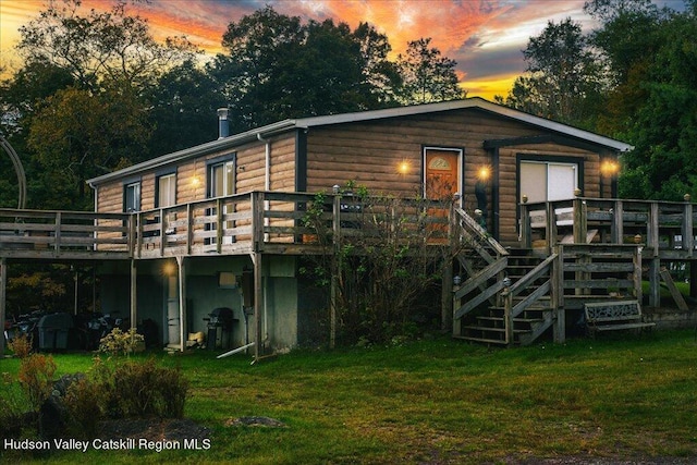 back house at dusk with a lawn and a wooden deck