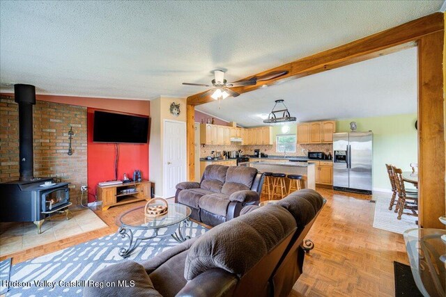 living room featuring a wood stove, ceiling fan, lofted ceiling with beams, brick wall, and light parquet floors