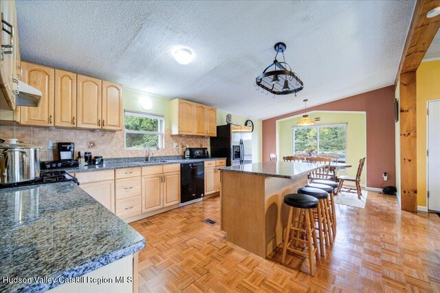 kitchen featuring black appliances, plenty of natural light, a center island, and lofted ceiling