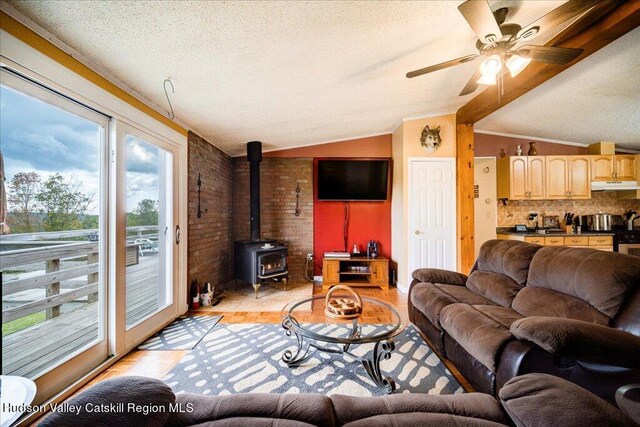 living room featuring a wood stove, ceiling fan, light hardwood / wood-style flooring, a textured ceiling, and vaulted ceiling