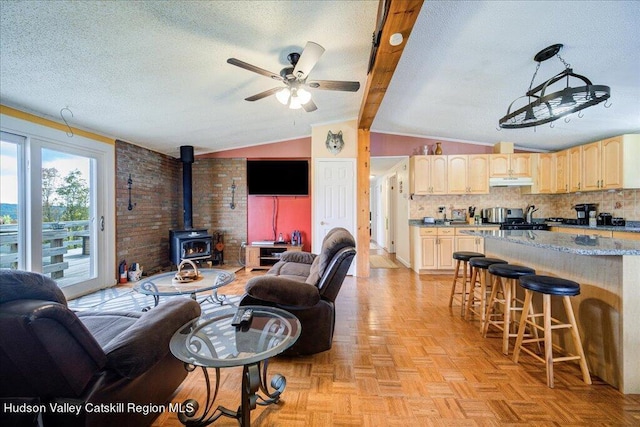 living room with brick wall, a textured ceiling, ceiling fan, vaulted ceiling with beams, and a wood stove