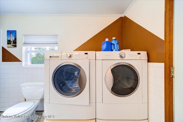 clothes washing area featuring crown molding, washing machine and dryer, and tile walls