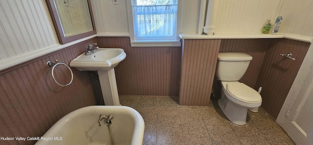 bathroom with a tub, wood walls, and toilet