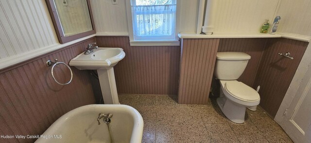 bathroom with a tub, wood walls, and toilet