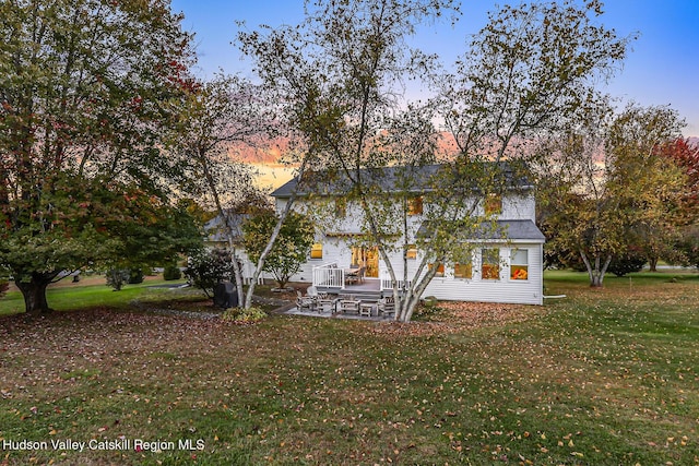 back house at dusk with a yard and a patio