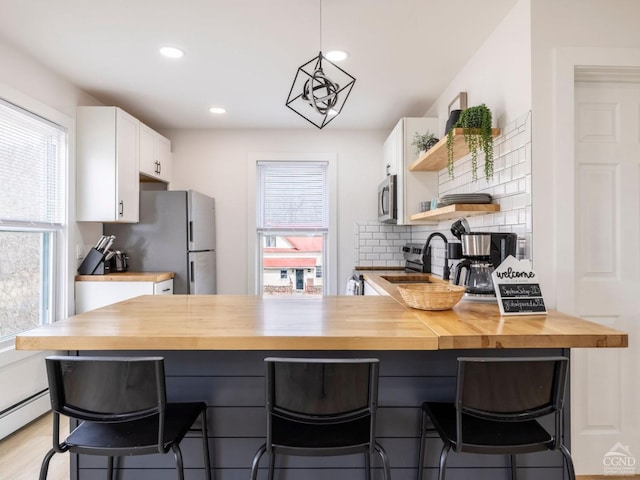 7614 Main St, Hunter, NY 12444 - kitchen featuring butcher block counters, stainless steel appliances, a peninsula, white cabinetry, and a breakfast bar