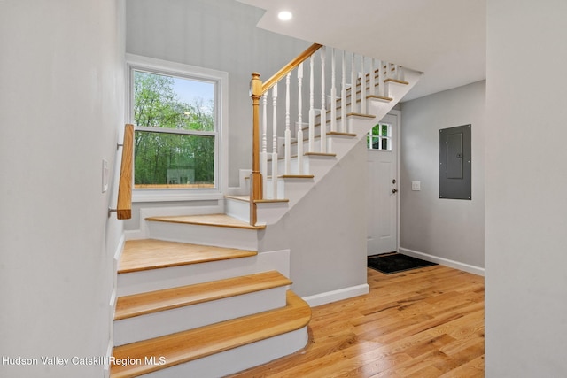 stairway with electric panel, wood finished floors, and baseboards