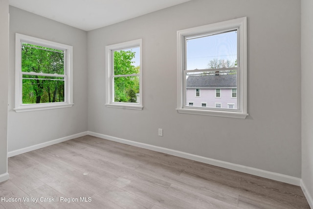 unfurnished room with healthy amount of natural light, wood finished floors, and baseboards