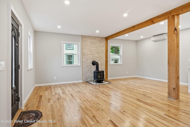 unfurnished living room featuring a wall unit AC, a wood stove, light wood-type flooring, recessed lighting, and baseboards