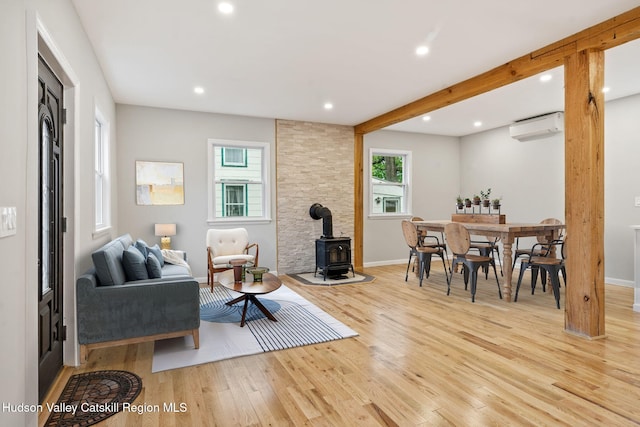 living room with an AC wall unit, a wood stove, light wood finished floors, recessed lighting, and baseboards