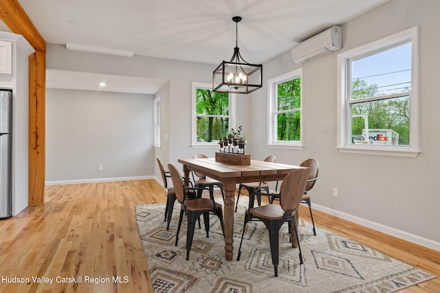 dining area featuring an AC wall unit, light wood-style floors, baseboards, and a chandelier