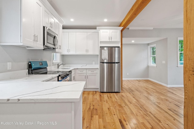 kitchen featuring appliances with stainless steel finishes, a sink, light wood-style floors, white cabinetry, and beam ceiling