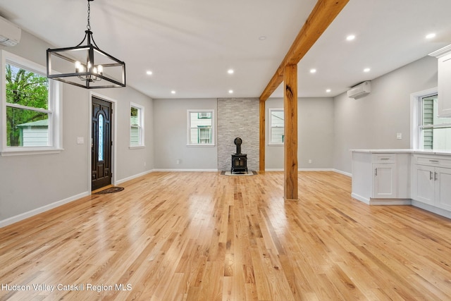 unfurnished living room featuring an AC wall unit, light wood-style flooring, a wood stove, a chandelier, and recessed lighting