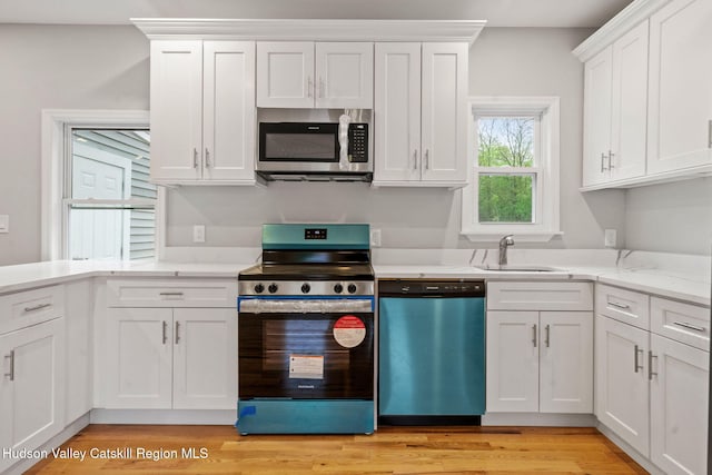 kitchen featuring stainless steel appliances, white cabinetry, a sink, light wood finished floors, and light stone countertops