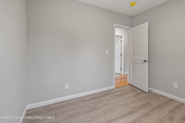 empty room with light wood-style floors, baseboards, and a smoke detector