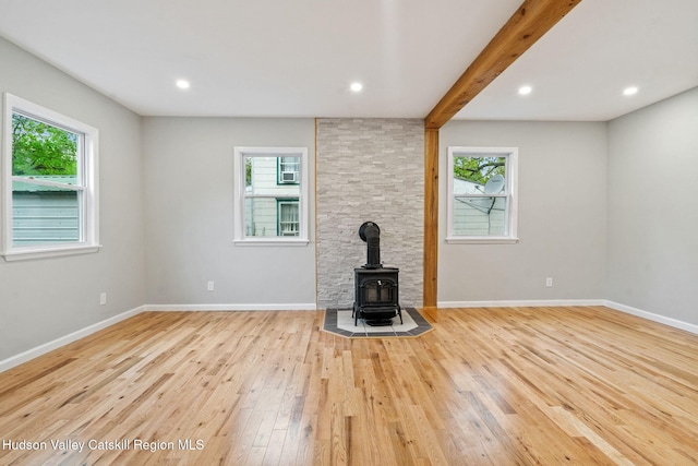 unfurnished living room with healthy amount of natural light, a wood stove, wood-type flooring, baseboards, and recessed lighting
