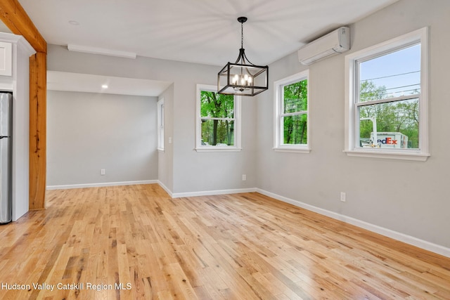 empty room with an AC wall unit, light wood-type flooring, baseboards, and a chandelier