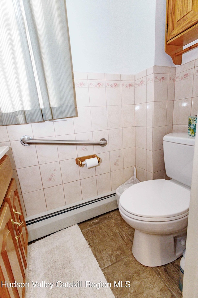 half bathroom featuring vanity, a baseboard heating unit, toilet, and tile walls