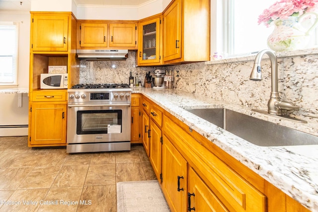 kitchen featuring a baseboard radiator, a sink, gas range, white microwave, and under cabinet range hood