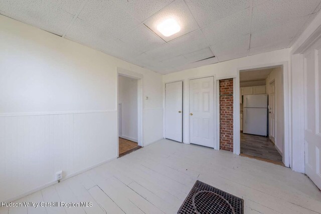 9 Hasbrouck Pl, Kingston, NY 12401 - unfurnished bedroom with freestanding refrigerator, a wainscoted wall, wood finished floors, a paneled ceiling, and two closets