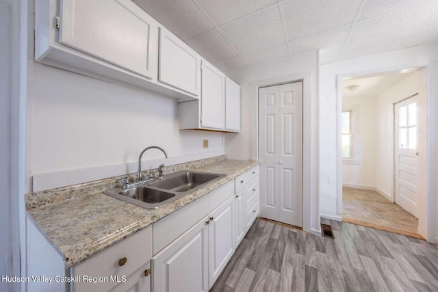 9 Hasbrouck Pl, Kingston, NY 12401 - kitchen with a sink, light wood-style flooring, white cabinets, a paneled ceiling, and baseboards