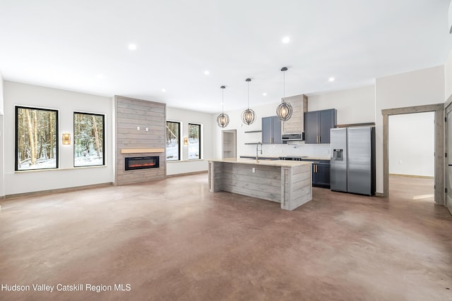 kitchen featuring stainless steel appliances, decorative light fixtures, concrete flooring, and an island with sink