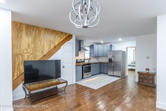 kitchen featuring appliances with stainless steel finishes, light wood-type flooring, gray cabinetry, wall chimney exhaust hood, and a notable chandelier