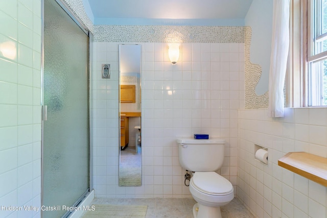 bathroom featuring tile patterned flooring, toilet, a shower with shower door, and tile walls