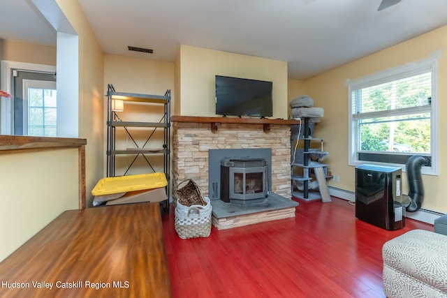 living room with hardwood / wood-style floors, a wood stove, a baseboard heating unit, and a healthy amount of sunlight