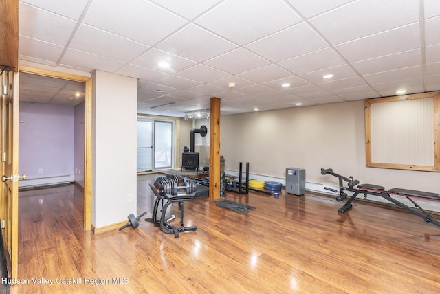 exercise area with a wood stove, baseboards, baseboard heating, and wood finished floors