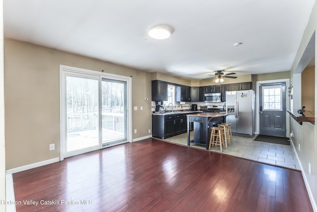 kitchen with baseboards, appliances with stainless steel finishes, wood finished floors, a kitchen bar, and a sink