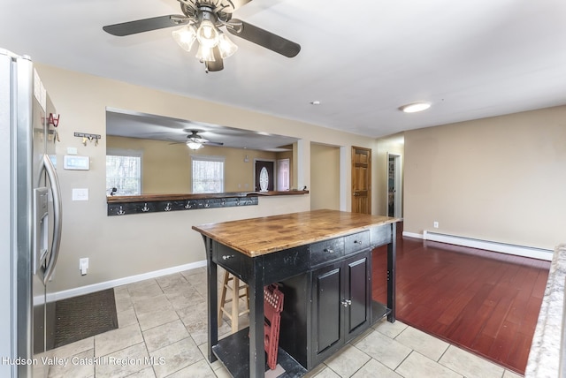 kitchen featuring light tile patterned flooring, dark cabinets, baseboards, baseboard heating, and stainless steel refrigerator with ice dispenser