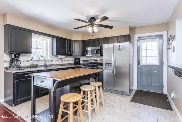 kitchen featuring a breakfast bar area, butcher block countertops, a sink, appliances with stainless steel finishes, and dark cabinetry