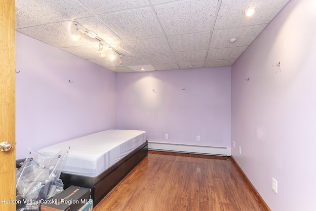 bedroom with a baseboard heating unit, a paneled ceiling, baseboards, and wood finished floors