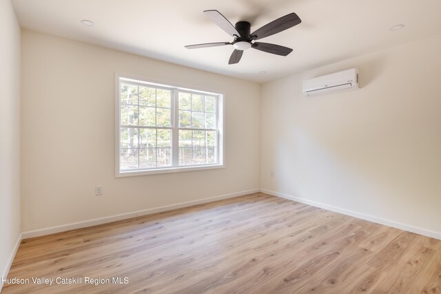 spare room featuring light wood finished floors, baseboards, and a wall mounted AC