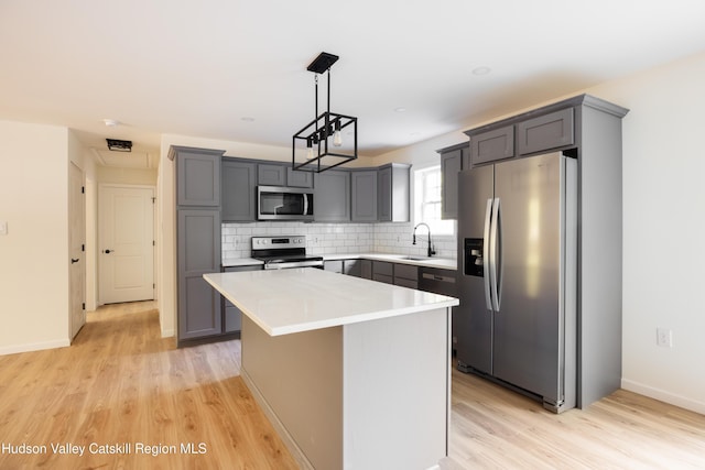 kitchen featuring a kitchen island, appliances with stainless steel finishes, gray cabinets, light countertops, and a sink