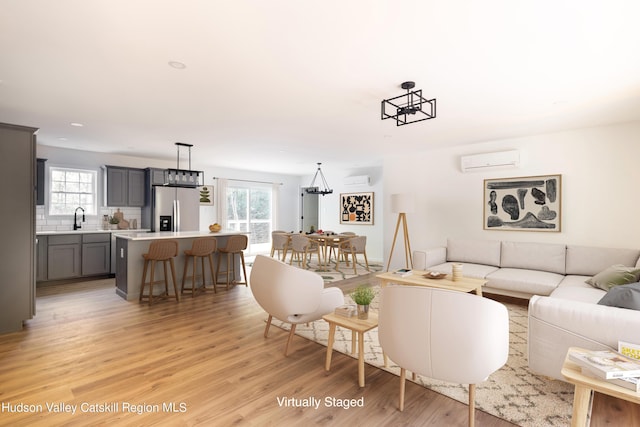 living area featuring light wood finished floors, a notable chandelier, a wealth of natural light, and a wall mounted air conditioner