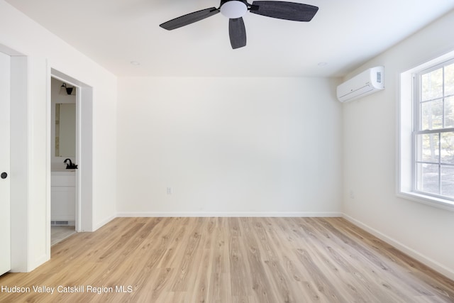 spare room featuring ceiling fan, an AC wall unit, light wood-style flooring, and baseboards