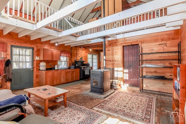 living area with wooden walls, a wood stove, wood finished floors, and beam ceiling
