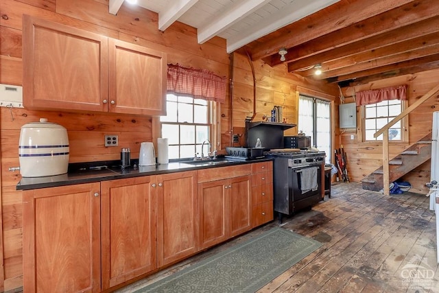 kitchen featuring wood walls, a sink, dark wood-style flooring, beam ceiling, and stainless steel range with gas cooktop