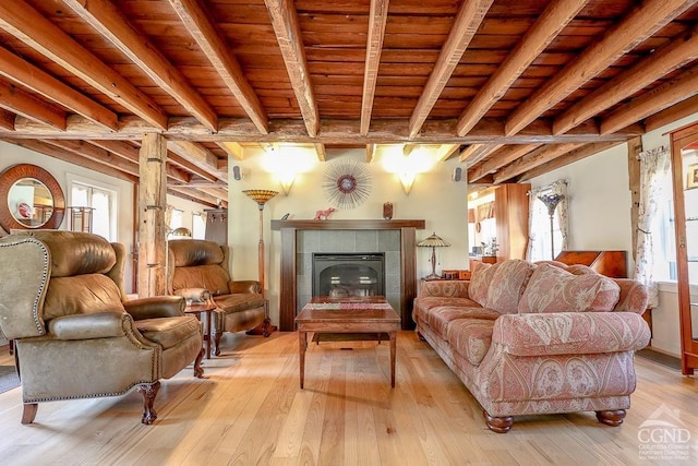 living area with light wood finished floors, beam ceiling, plenty of natural light, wooden ceiling, and a tile fireplace
