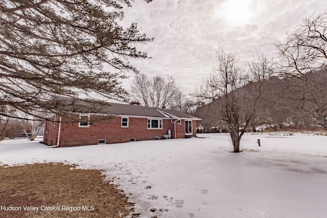 snow covered property with brick siding and a chimney