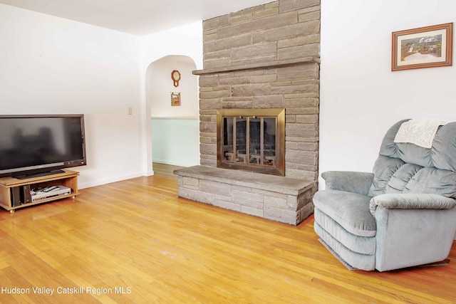 living room with arched walkways, a stone fireplace, wood finished floors, and baseboards